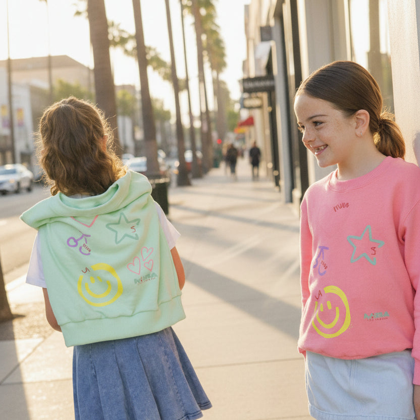 Three young girls standing outdoors, wearing matching outfits with a smile.
