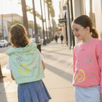 Three young girls standing outdoors, wearing matching outfits with a smile.