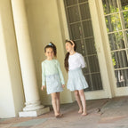 Two young girls standing on a porch with columns and a lantern.
