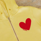 Yellow hoodie with a red heart and 'MIRA' logo on a stone surface