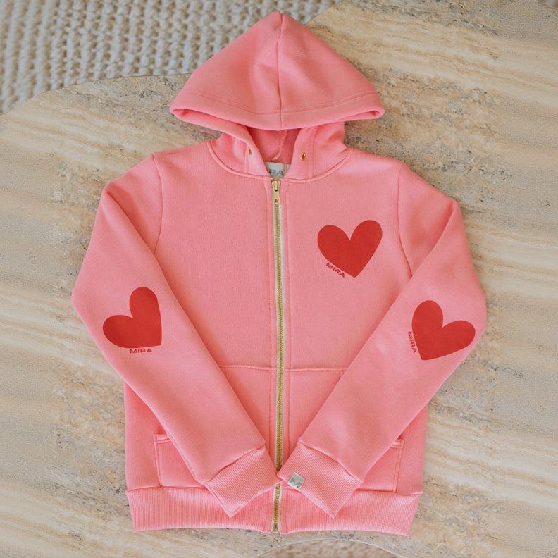 Pink hoodie with red heart designs on a textured surface