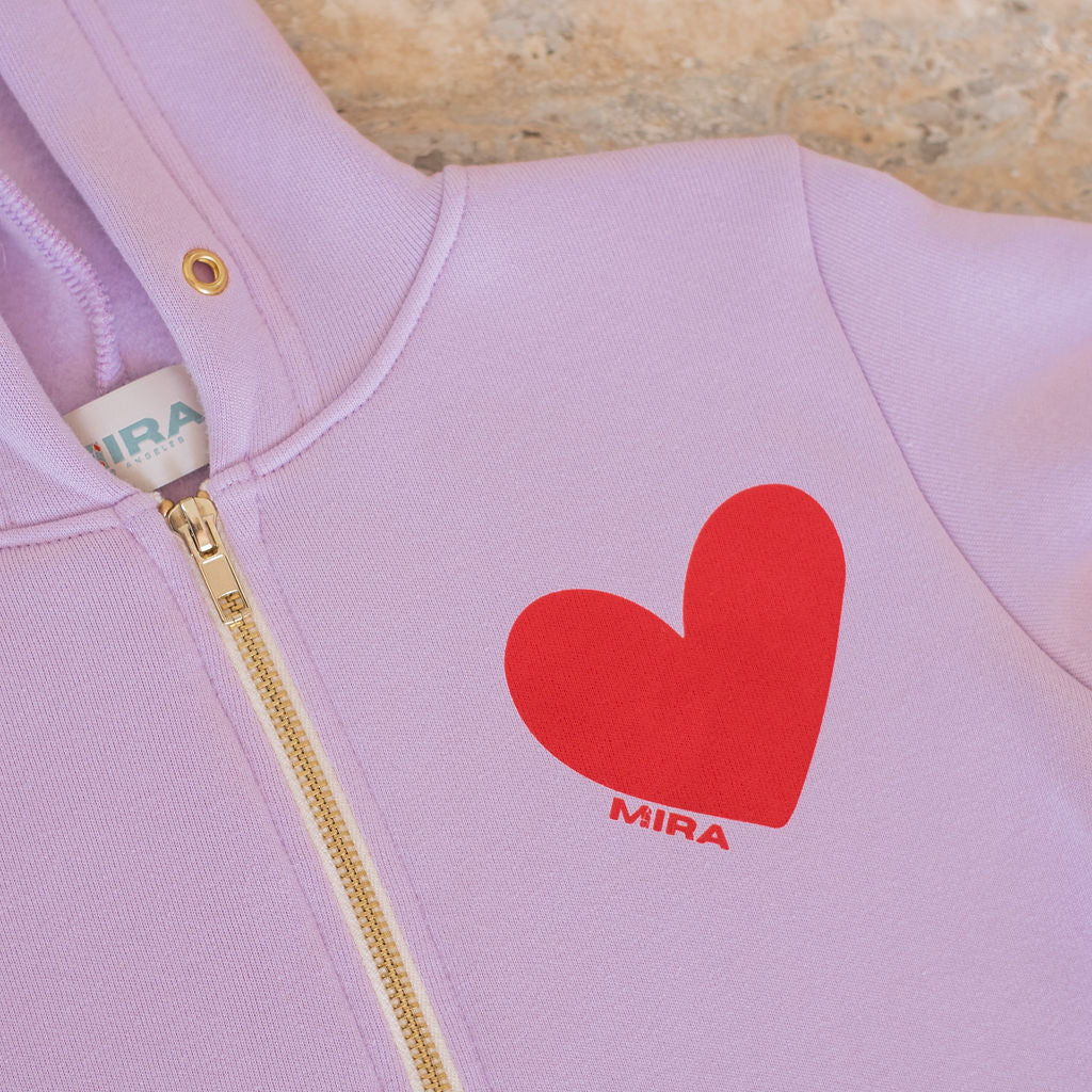 Pink hoodie with a red heart and 'MIRA' logo on a wooden surface
