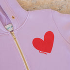Pink hoodie with a red heart and 'MIRA' logo on a wooden surface