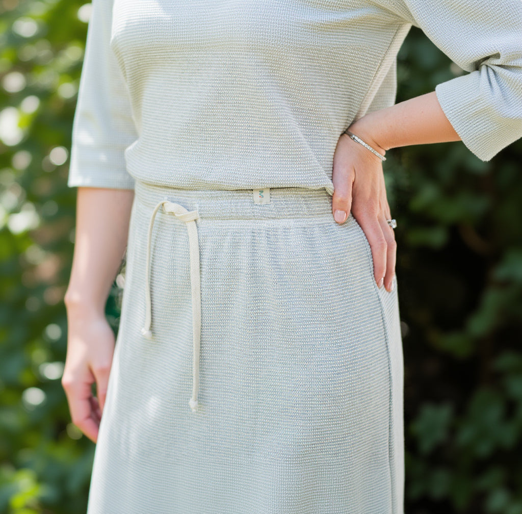 Person wearing a light-colored knit top and skirt with a blurred background