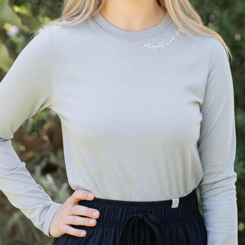 Person wearing a light gray long-sleeve shirt and black pants outdoors.