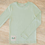 Light green long-sleeve shirt with a brand label on a beige surface
