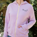 Person wearing a light purple hoodie with a logo on the chest, standing outdoors.