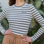 Person wearing a striped long-sleeve shirt and beige pants with a blurred green background