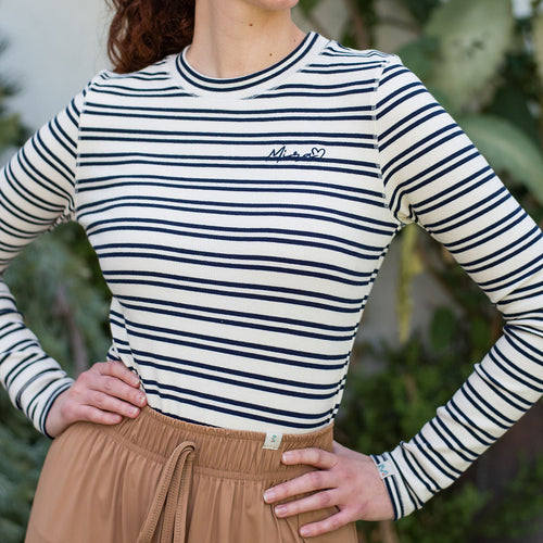 Person wearing a striped long-sleeve shirt and beige pants with a blurred green background