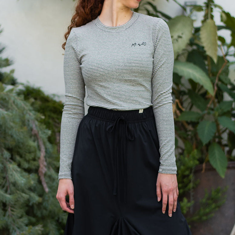 Woman wearing a gray long-sleeve top and black skirt with blue sneakers outdoors.