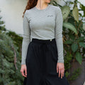 Woman wearing a gray long-sleeve top and black skirt with blue sneakers outdoors.